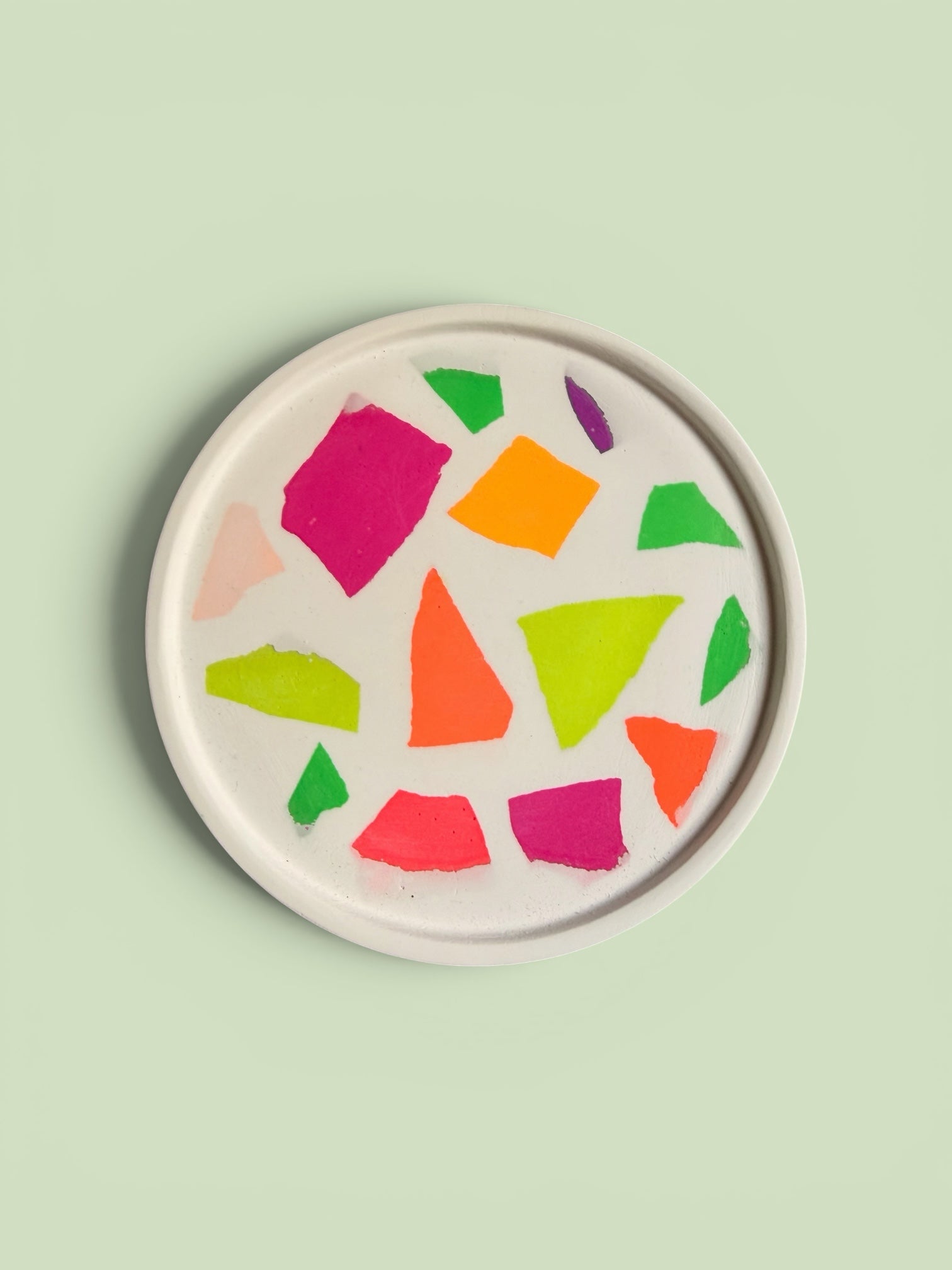 Craft and Babble circular white serving tray with a vibrant neon terrazzo pattern on a light green background.